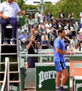 a man in a blue shirt is standing in front of a perrier sign