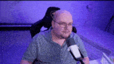 a bald man wearing glasses and a plaid shirt is sitting in front of a microphone in a purple room .
