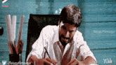 a man in a white shirt sits at a desk with a pen in his hand
