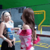two women are standing next to each other in a parking lot with a green screen in the background .