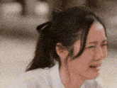 a close up of a woman 's face with a ponytail crying .