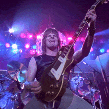 a man is playing a guitar in a dark room with purple lights behind him