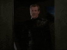 a man in a black leather jacket is standing in a dark room .