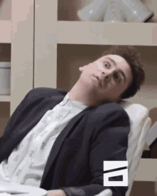 a man in a suit is laying on a chair with his head on the arm rest .