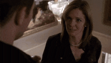 a woman wearing a pearl necklace and earrings talks to a man