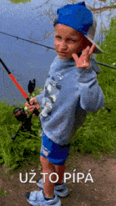 a young boy is holding a fishing rod and giving a peace sign in front of a lake