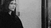 a black and white photo of a woman in a fur coat looking at the camera .