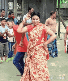 a woman in a floral dress is dancing in front of a group of people with the word alamin on the bottom right