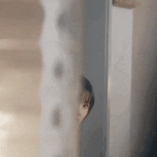 a woman is peeking out from behind a door and looking at the camera .