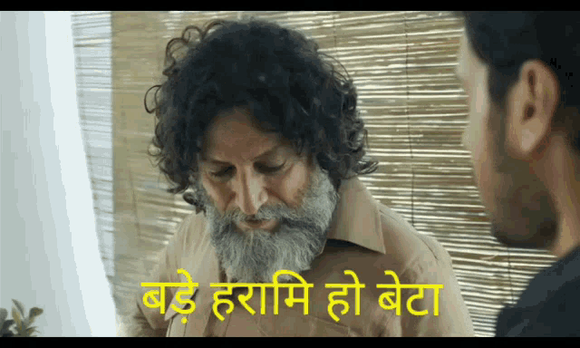 a man with curly hair and a beard is talking to another man with a caption in a language other than english