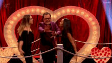 a man and two women are standing in front of a heart shaped sign .