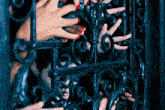 a woman with red nails is peeking through a wrought iron fence