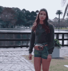 a woman wearing shorts and a sweater is standing in front of a lake .