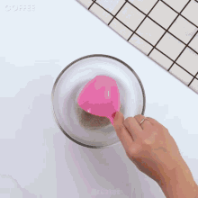 a person holding a pink spoon in a glass bowl with coffee written on the bottom