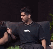 a man in a black t-shirt is sitting on a couch talking to another man .