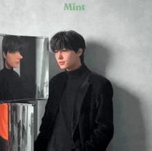 a young man in a black suit is standing in front of a mirror with the word mint on the bottom