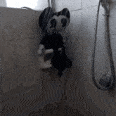 a black and white stuffed cat is hanging from a shower head
