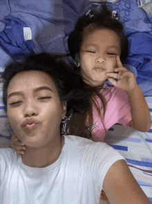 a woman and a little girl are laying on a bed and making faces