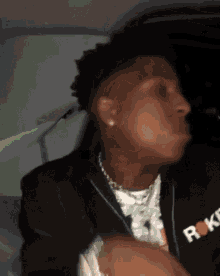 a man wearing a black jacket and a necklace is sitting in a car and making a funny face .
