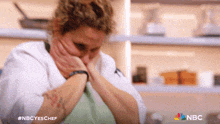 a woman in a chef 's uniform is covering her mouth with her hands and the nbc logo is visible in the corner