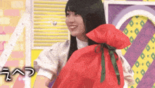 a young woman is holding a red bag with a green ribbon .