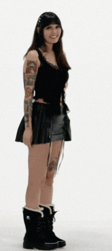 a woman with tattoos on her arms is wearing a black skirt and boots