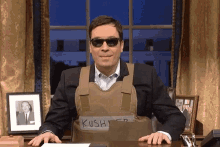 a man sitting at a desk with a vest that says kush on it