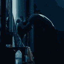 a man is washing his face in a dark room with a bottle of water next to him