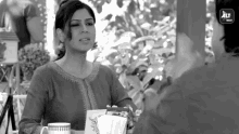 a woman is sitting at a table with a cup of coffee and talking to a man .