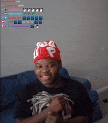 a young man wearing a red supreme hat is sitting on a couch