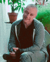 a man in a gray hoodie sits in front of a window