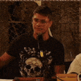 a man wearing glasses and a black shirt with a skull on it stands in front of a microphone