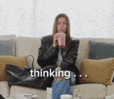 a woman is sitting on a couch drinking a smoothie and the word thinking is on the screen