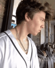 a young man wearing a necklace and earrings looks to his left