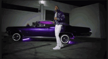 a man standing next to a purple car with purple lights