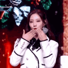 a woman in a white jacket is blowing a kiss on a stage