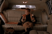 a young boy is sitting in the back seat of a lincoln limousine eating pizza