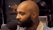 a bald man with a beard is sitting in front of a microphone in a room .