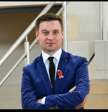 a man in a blue suit and black tie with a red ribbon on his pocket
