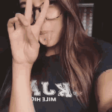 a girl wearing glasses and a black shirt with the letter l on it giving a peace sign