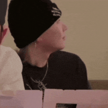 a man wearing a black beanie is sitting at a table with a box of pizza .