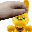 a person is petting a yellow teddy bear with green eyes and a purple bow tie .