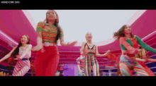 a group of women are dancing together in a room with a pink background .