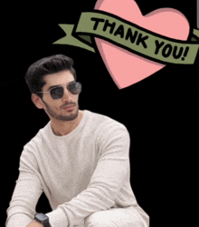 a man wearing sunglasses sits in front of a thank you heart