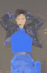 a man wearing a microphone and a jacket is sitting in front of a blue background .