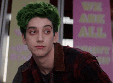 a young man with green hair stands in front of a sign that says " we all "