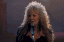 a woman is singing into a microphone while a man in a cowboy hat stands behind her .