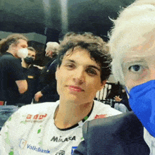 a man wearing a mikasa shirt takes a selfie with another man
