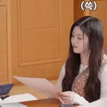 a girl is sitting at a table holding a piece of paper and a pen
