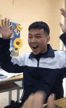 a young man is sitting at a desk with his arms in the air
